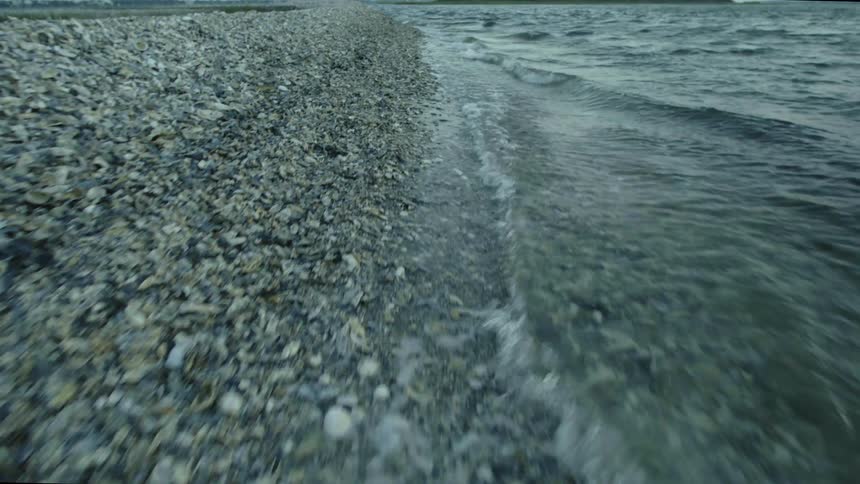 Close up of small waves gently washing over the pebbles piled up on a beach shoreline