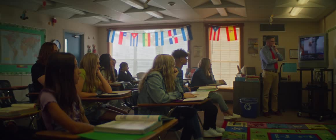 Teacher and high school students watch video playing on television in classroom