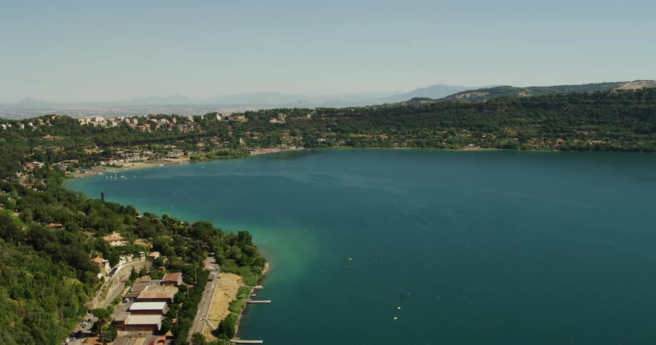 Town hugs shore and near by hills overlooking blue ocean water as mist obscures mountains on the horizon
