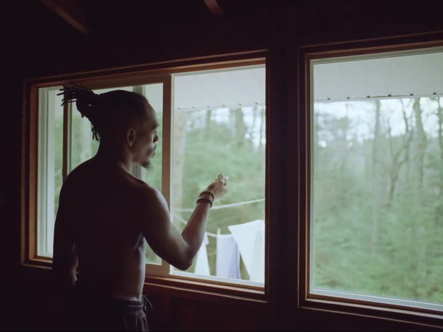 A man is standing in a room near windows with a butterfly on his hand as he watches it move