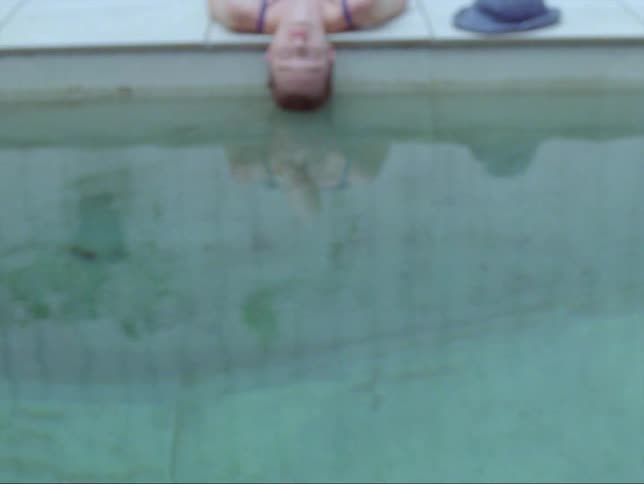 A female is resting by a pool during midday