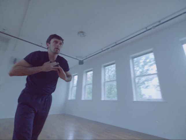 Male dancer practices in dance studio while looking into large wall sized mirror
