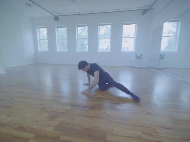 A man is dancing gracefully on the wooden floor of the dance studio
