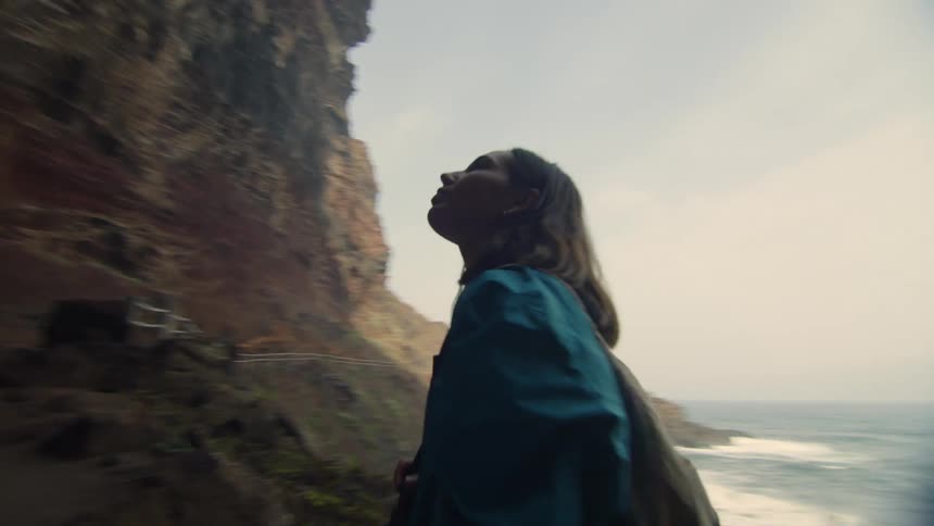 A woman with a camera has hiked up to a cliff on the coast