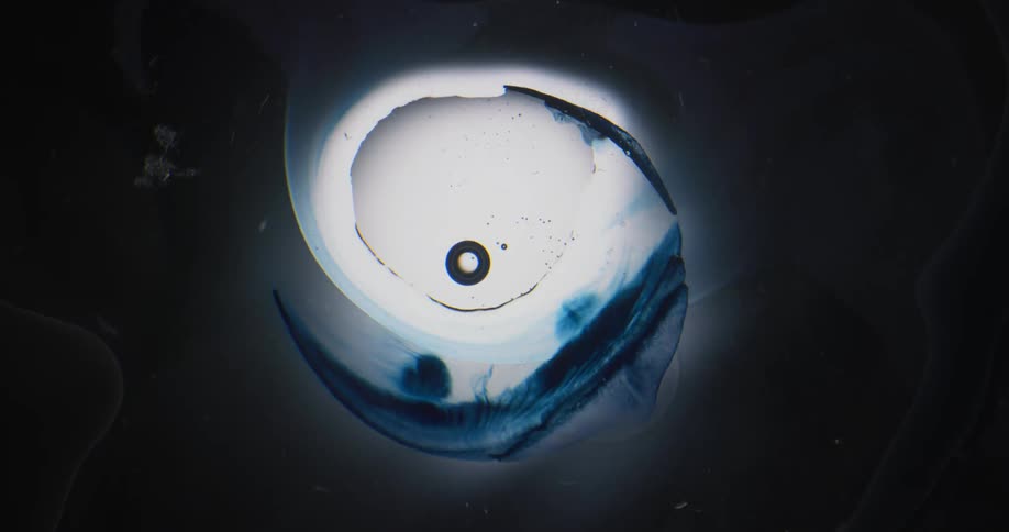 Clear liquid moves over a blue semi circular object and the color runs as spheres float over the area