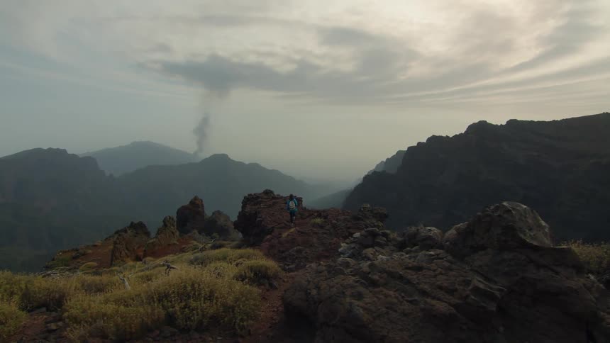 A girl hiking climbs up a large rock in the hills