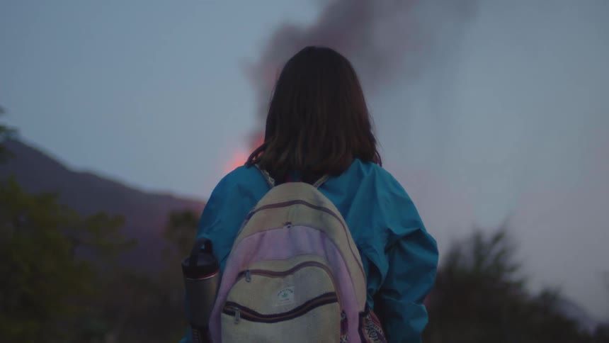 A girl stands and watches as a large fire burns on a hill