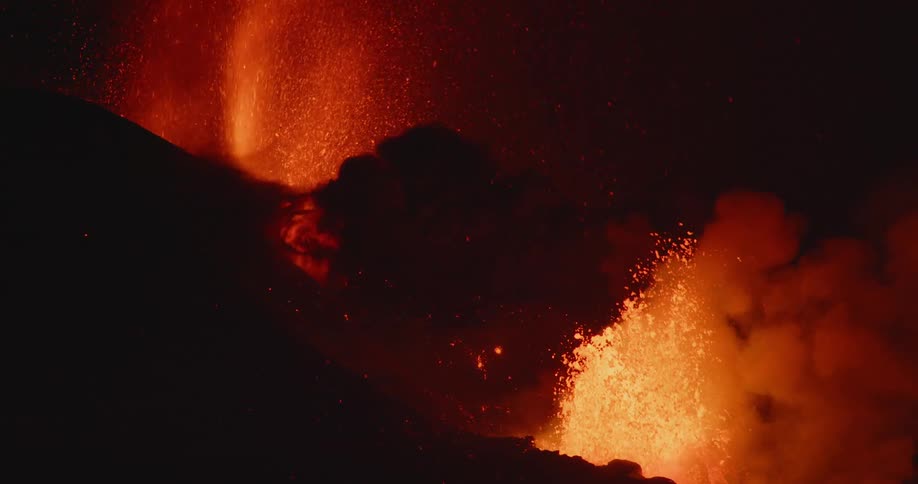 Lava and thick black clouds of smoke and ash violently erupting from a volcano at night