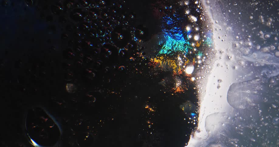 Bubbles move and reflect colors as they move through the darkness then glow turquoise as they reach the white area