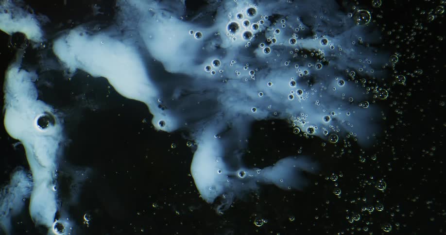 Bubbles are resting in a foamy white liquid as clear spheres float above and reflect the light