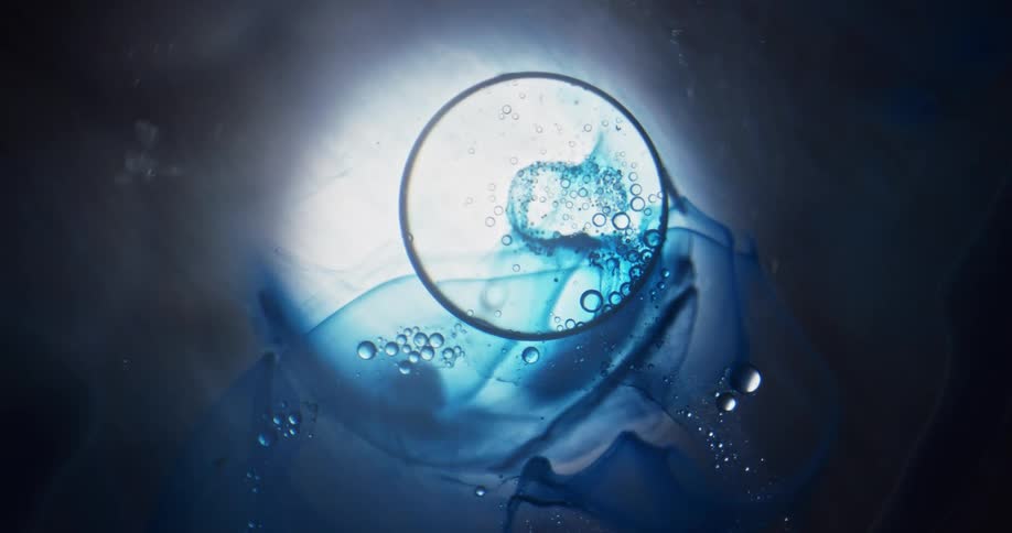 A fuzzy white light glows and bubbles move in an organic blue substance as a large sphere moves over and reflects the colors