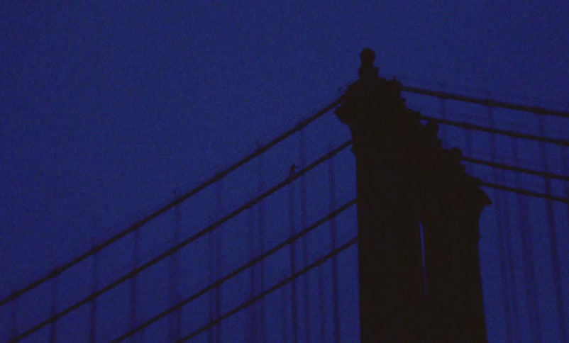 Person climbs sloping support toward tower of suspension bridge and is silhouetted against the night sky