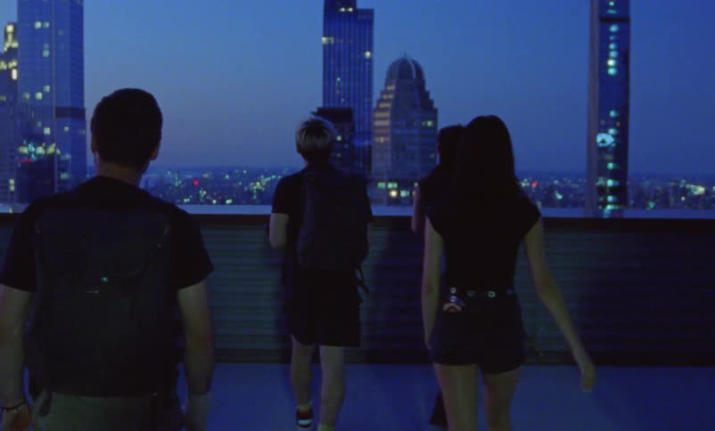 Group of young people carrying filming equipment on a building roof looking at the city skyline