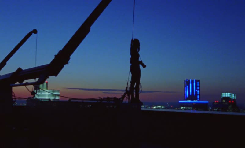 Silhouette of a woman standing at the edge of the roof of a skyscraper with a camera