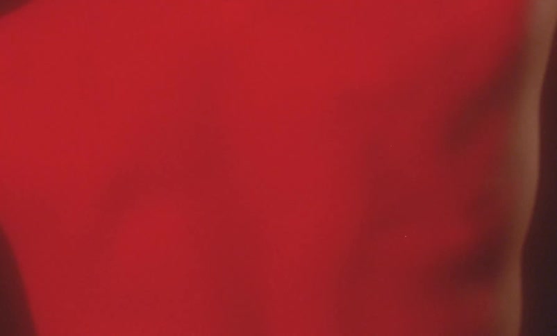 Red light shines on the bare back of a person moving their arms in the darkness