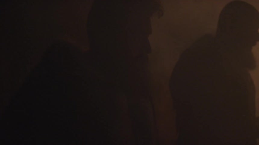 Two men standing in the dim light of a fire