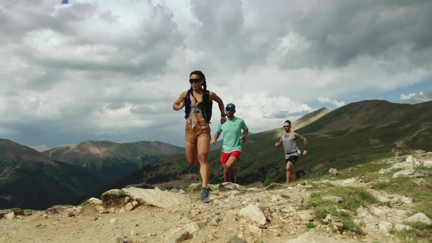 Three runners sprinting up a mountainside on a cloudy day