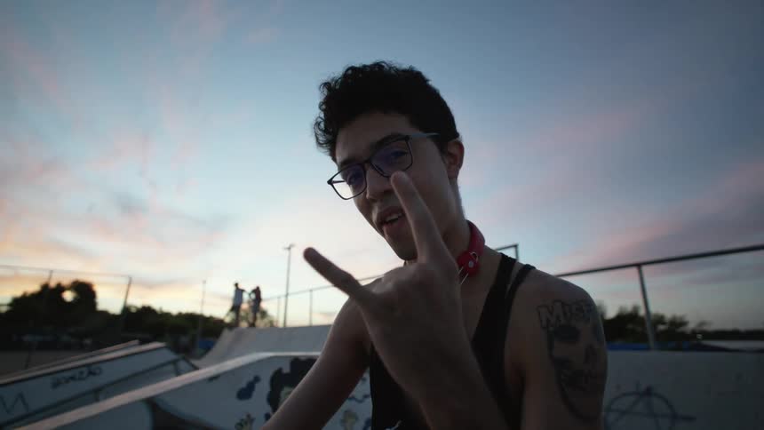 A young man with tattoos giving rock on fingers at a skate park