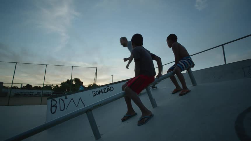 Two kids watch a man skateboard down a ramp at a park