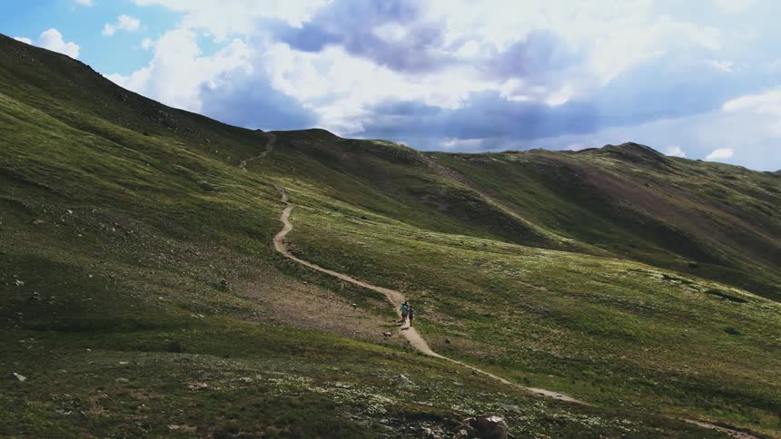 Three people jog along dirt path leading up green slope