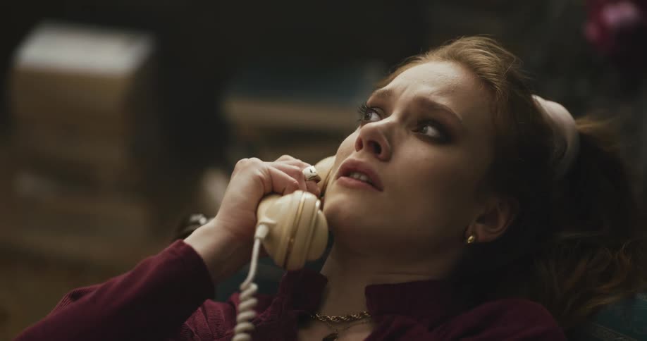 A woman sitting with her head back talking on a corded phone looking shocked and distraught