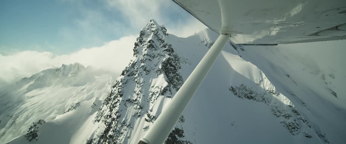 The wing and window of a small plane flying over snow covered mountain ridge