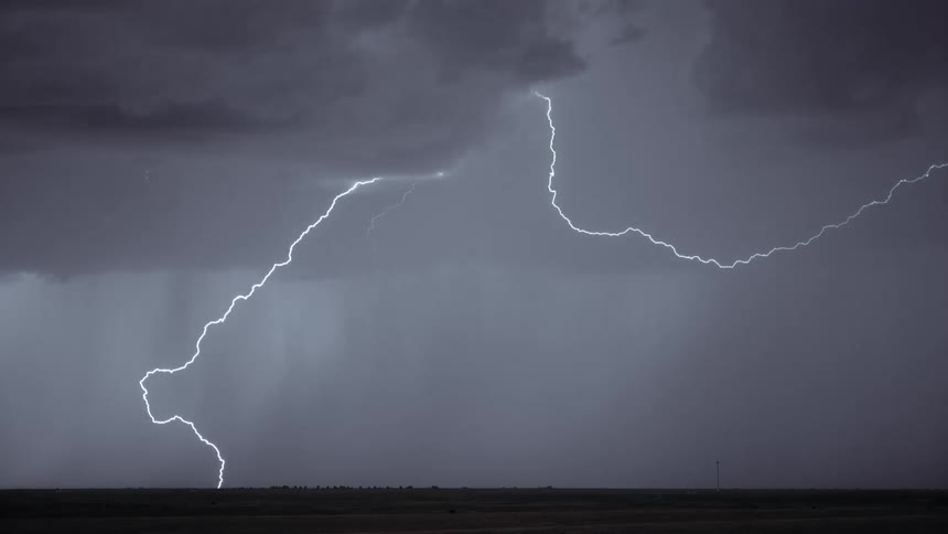 Dark storm clouds hang over a hazy foggy sky and lightning bolts flash and spread across the sky
