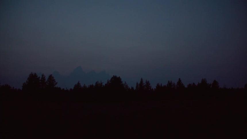 A large area of land covered with trees being silhouetted against the sky at dusk