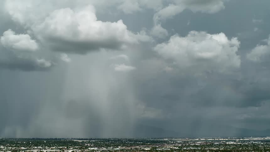 Electric storm and rain falling from storm clouds over a small town at daytime