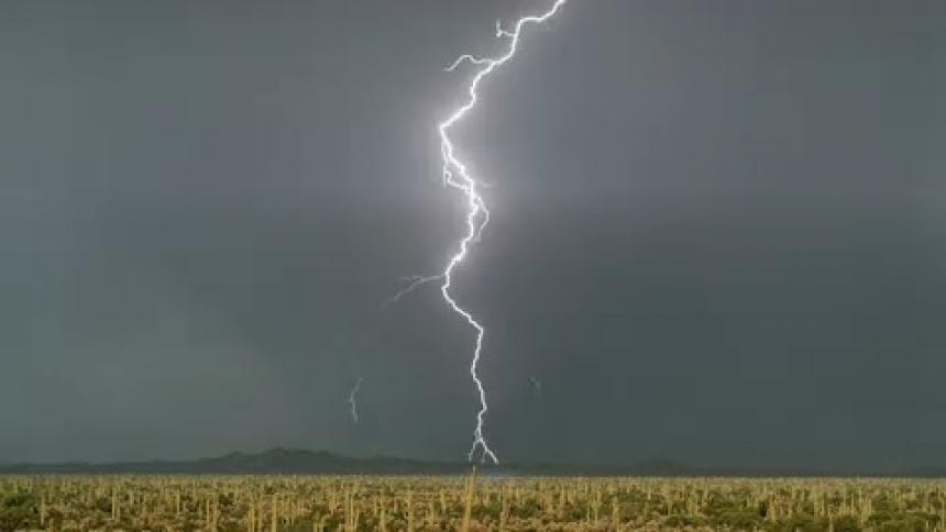 Lightning flashes across a darkening sky over a field and there are mountains in the distance