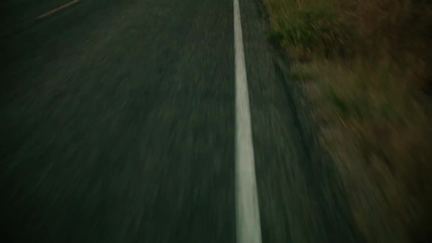Cyclist pedals along highway through fences pastures passing car going in the opposite direction