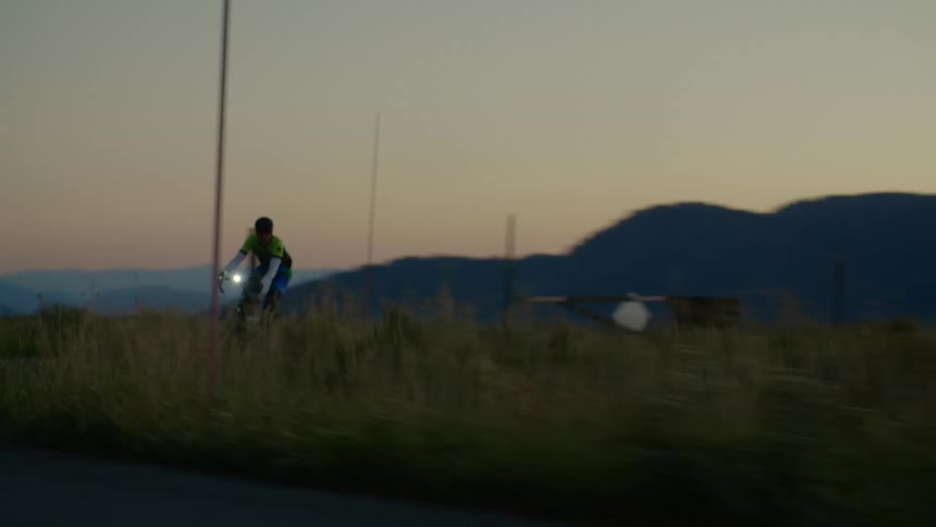 A cyclists rides a bicycle along a road through the countryside in the evening