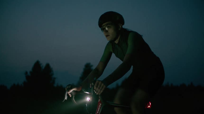 Female cyclist rides bicycle on country road in the countryside at dusk