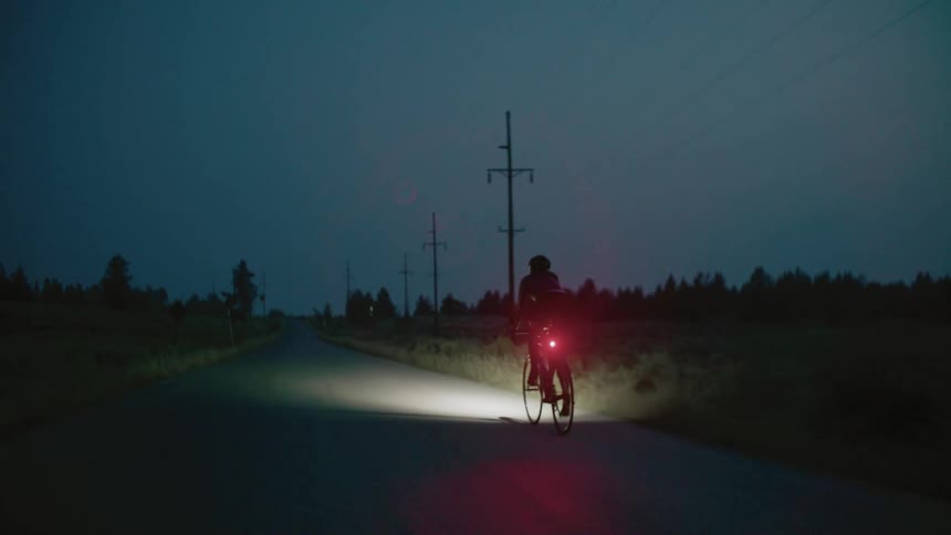 Female cyclist pedals along highway through countryside at night