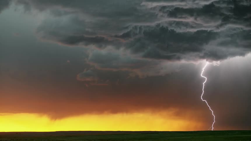 Dark storm clouds roll in over a yellow sky as lightning strikes the ground