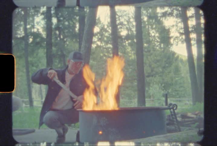 A man tending a fire in a fire pit in the forrest shot on super 8mm film