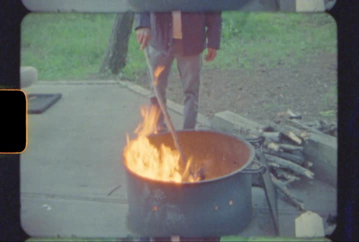 A man tending a fire in a fire pit while camping in a forest shot on 8mm film