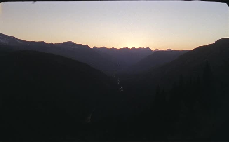 Sun sits on horizon turning sky red and mountains and trees into silhouettes in glacier national park shot on 16mm film