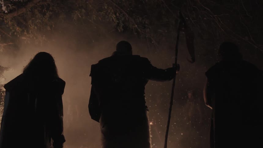Three people stand by a fire one raises a flag