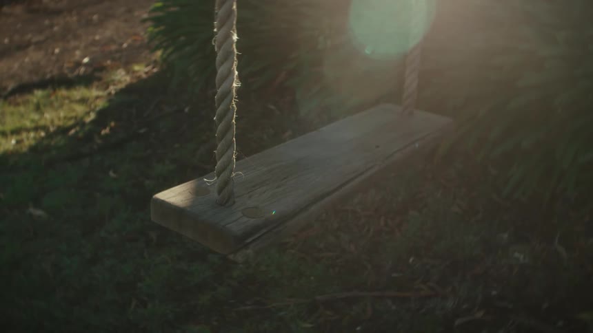 Sunlight shines as a swing made of rope and wood moves in the breeze