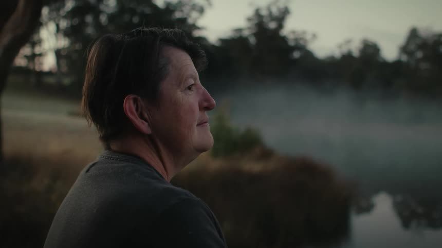 A woman deep in thought while overlooking a lake on a foggy morning