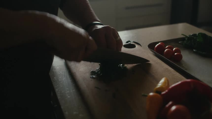 Woman with gray sweatshirt chops vegetables on cutting board in the kitchen