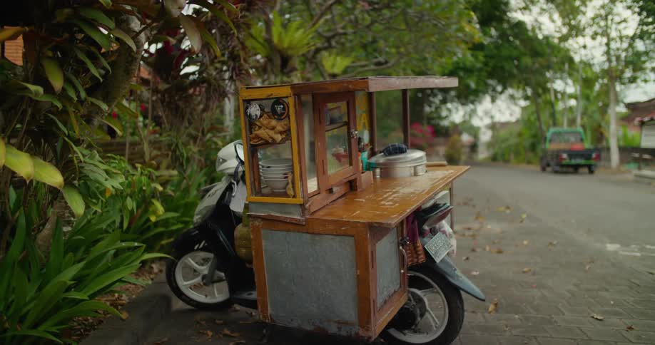 A motorcycle food cart parked on the side of a road on a small town