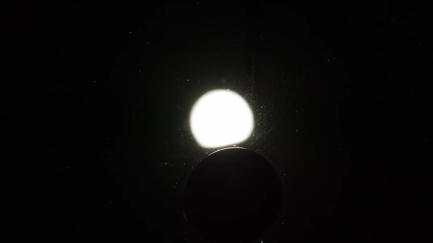 A white orb is shining brightly and a black sphere moves over it causing an eclipse