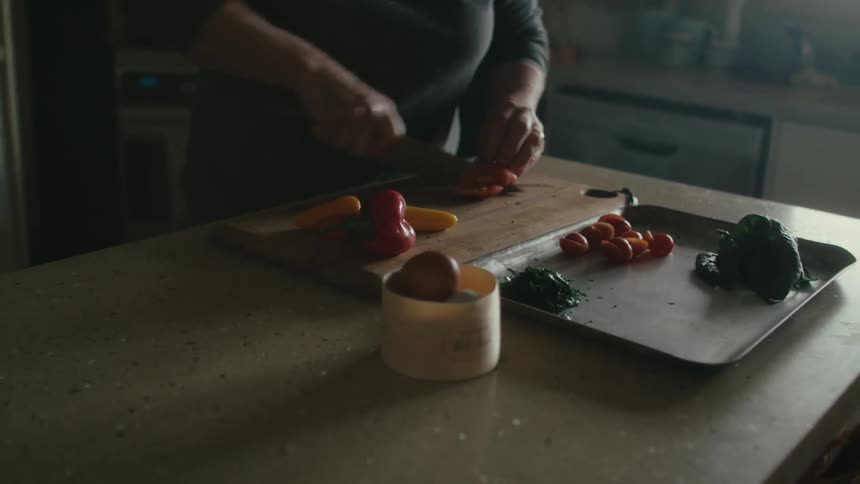 A woman slicing up vegetables on a wood cutting board at home