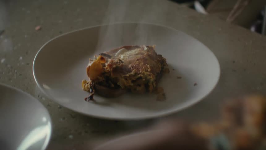 A person serves portions of steaming food on white ceramic dishes with a spatula