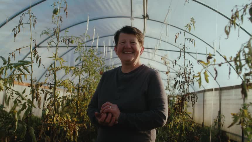 Happy woman with gray sweatshirt looks at camera in greenhouse smiling