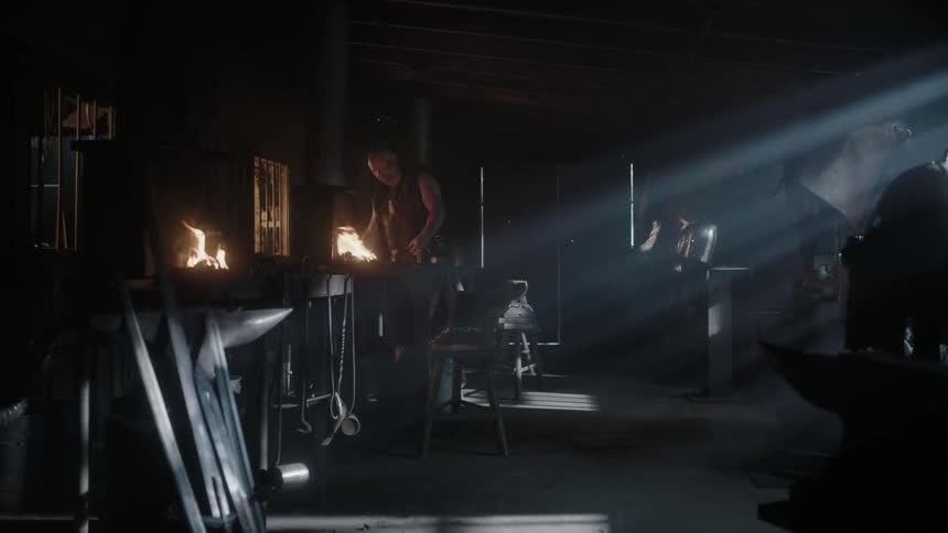 A blacksmith is arranging his tools and tending to his fire