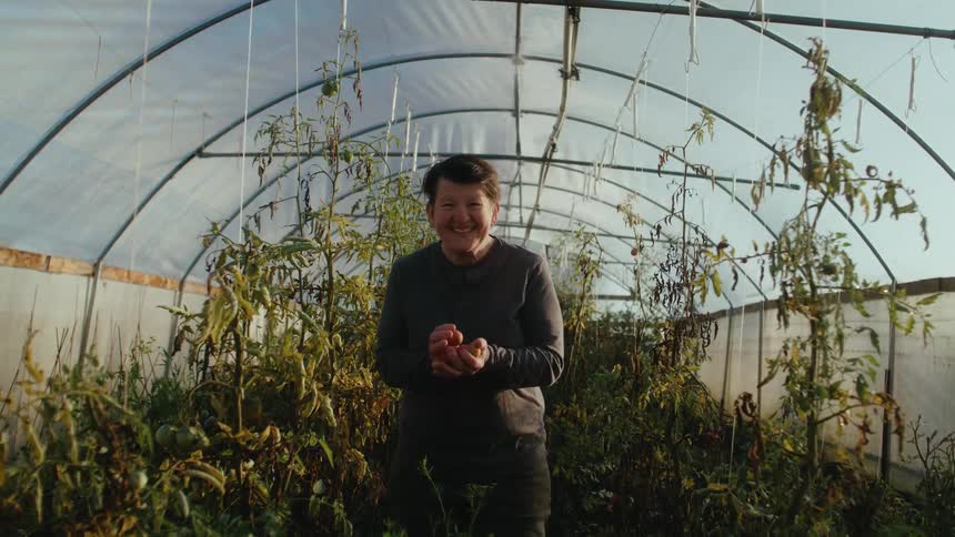 A woman smiling while holding produce in a greenhouse