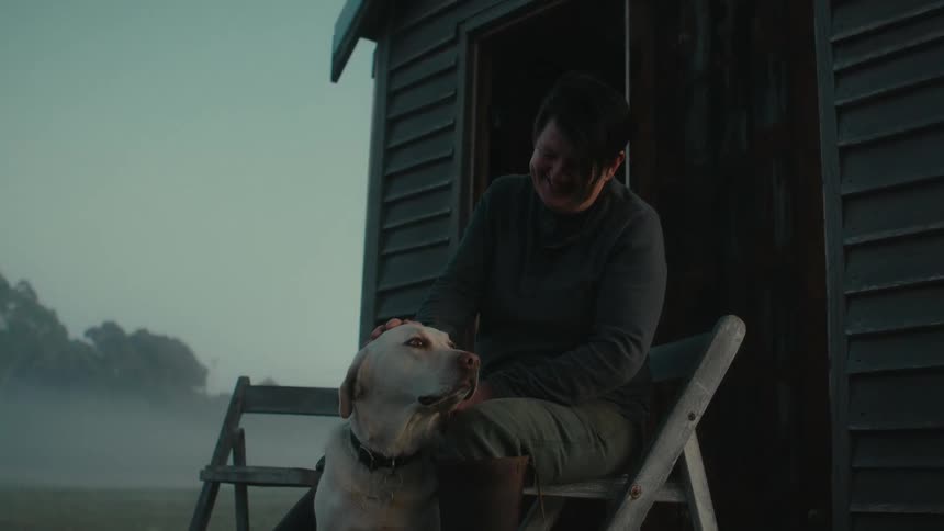 Woman sitting on a folding chair petting her dog at morning in the countryside